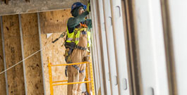 Person in a safety vest and hard hat standing on a ladder at a construction site. 