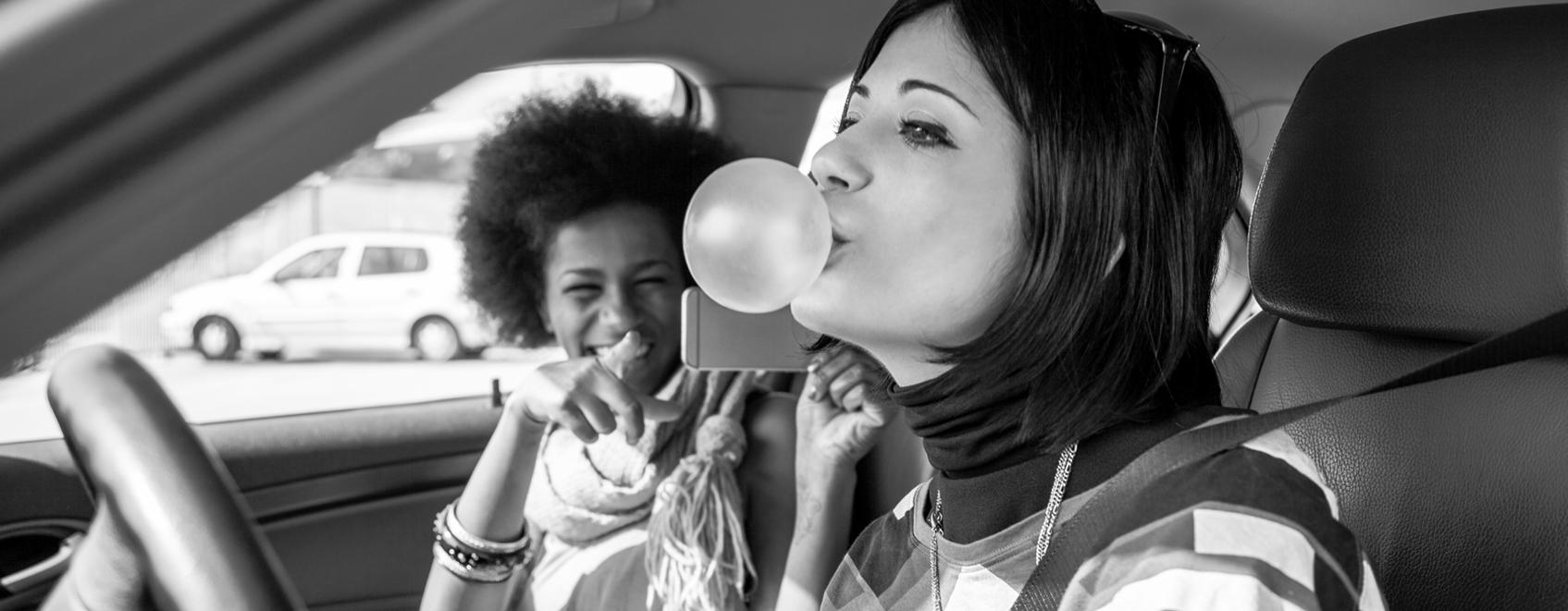 two teenagers in front seat of car laughing with phone