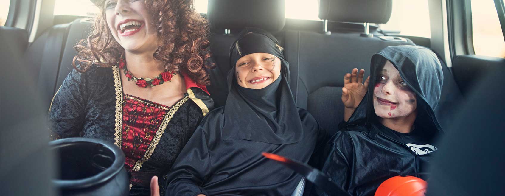 three children in Halloween costumes, laughing in the backseat of a car