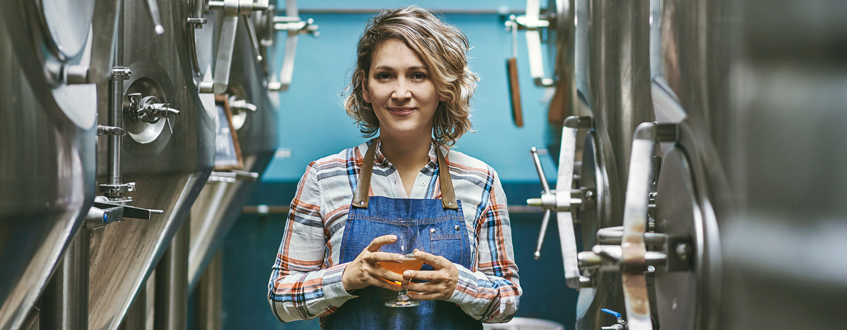 Person holding beer glass in brewery. 