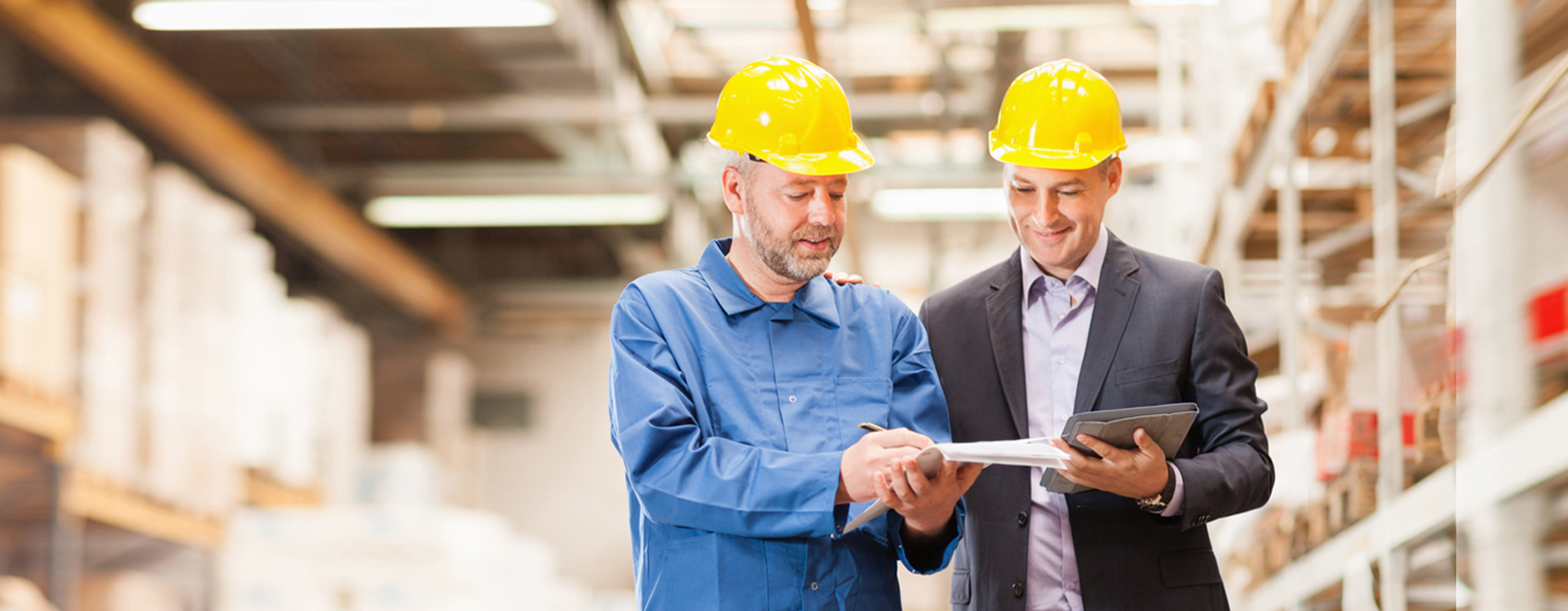 2 people in hardhats, reviewing papers in warehouse