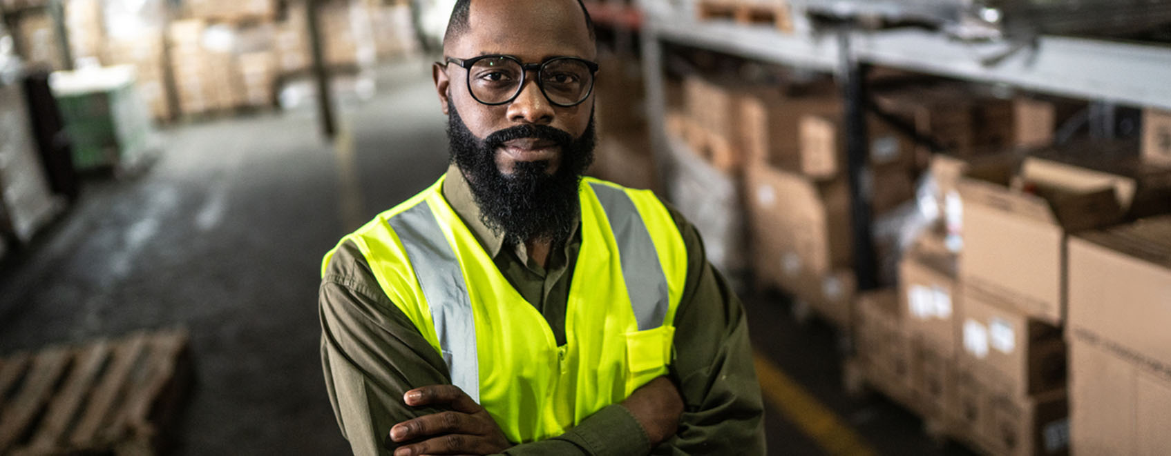 Supervisor standing among warehouse with safety gear.