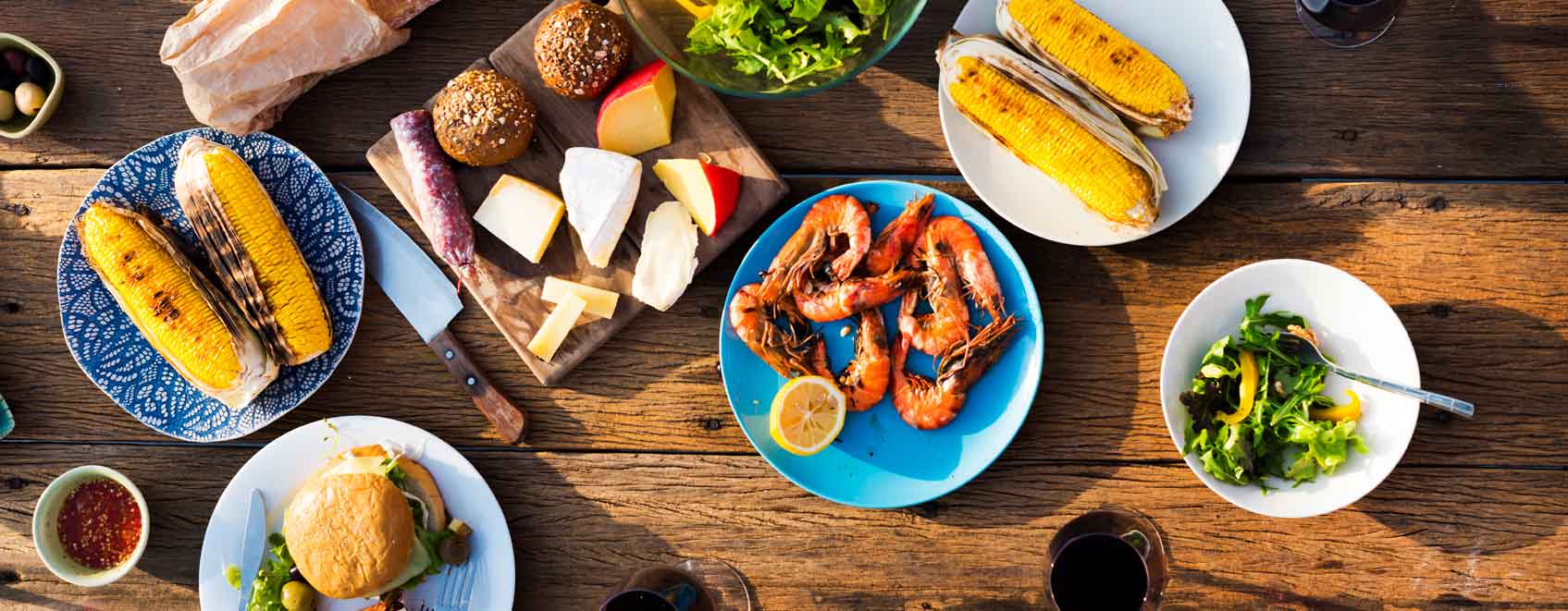 Overhead view of assorted bbq food on plates at a picnic table.