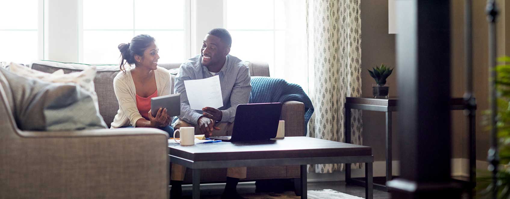 Couple sitting on sofa in their home talking and reviewing homeowners insurance basics.