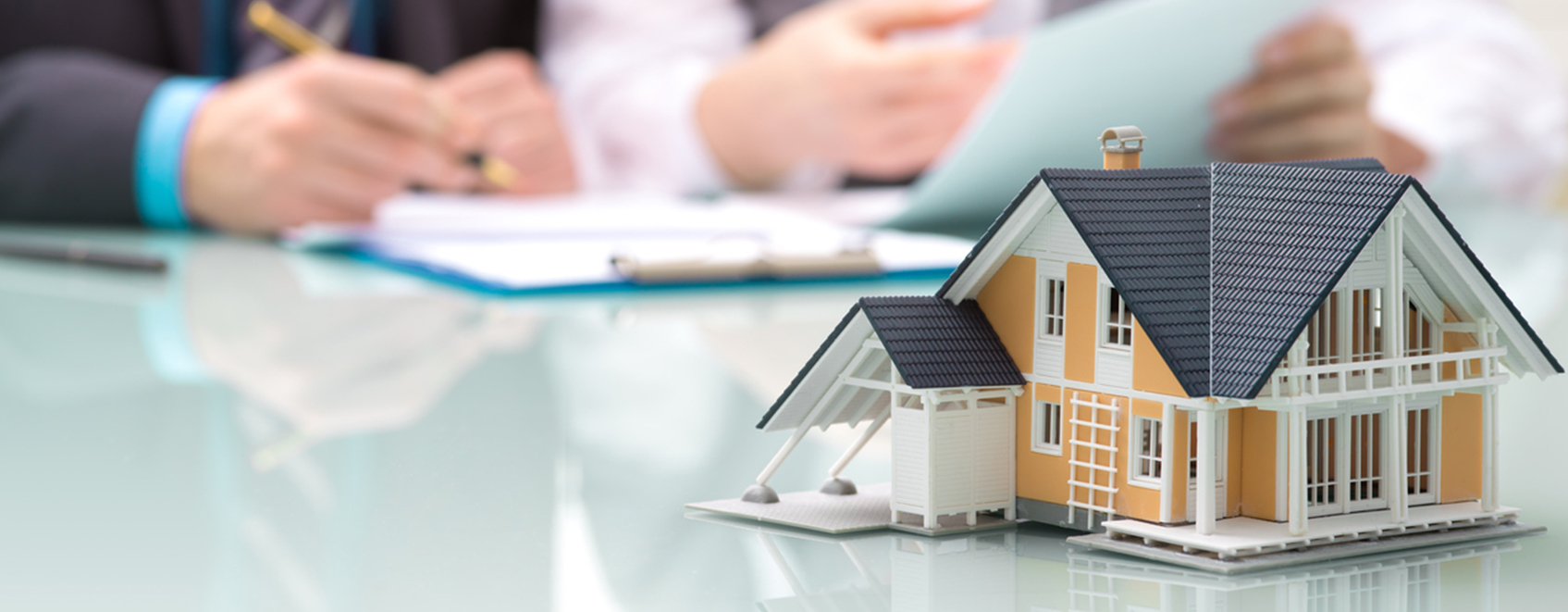 Small model of home on a table, with hands of people writing in the background.