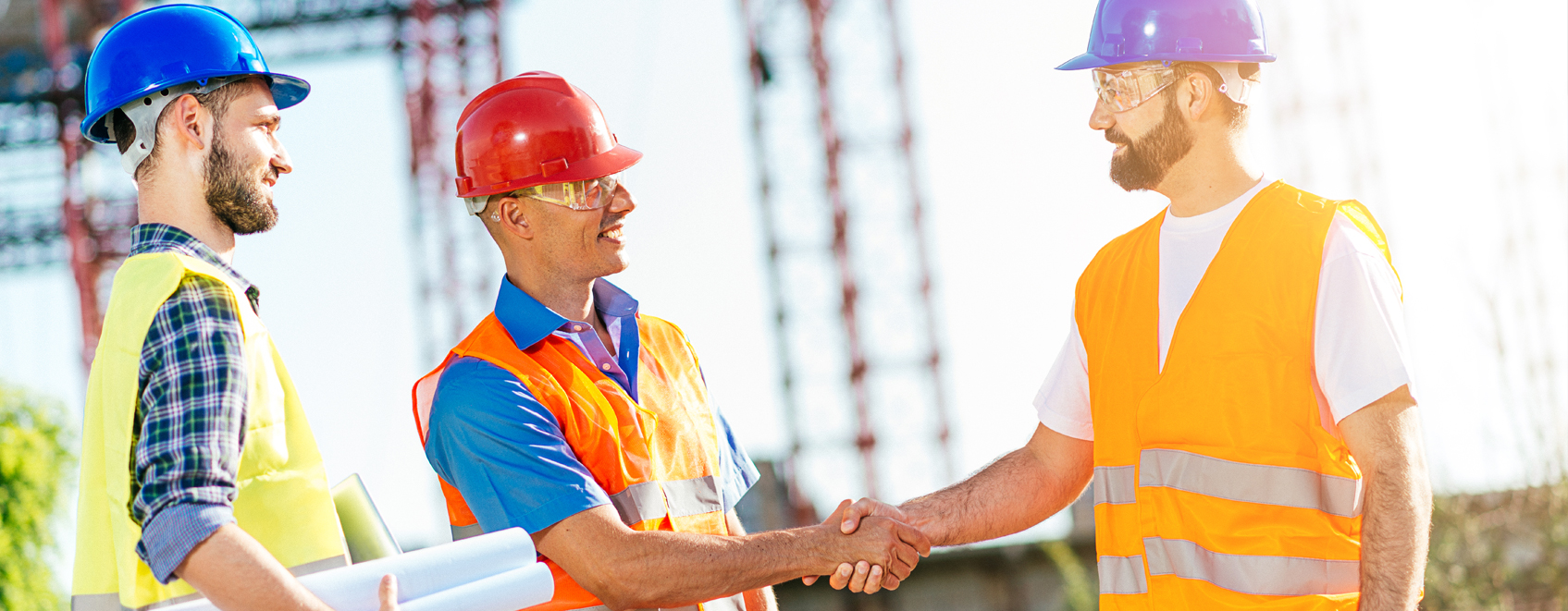 Team of contractors wearing safety equipment and shaking hands near job site