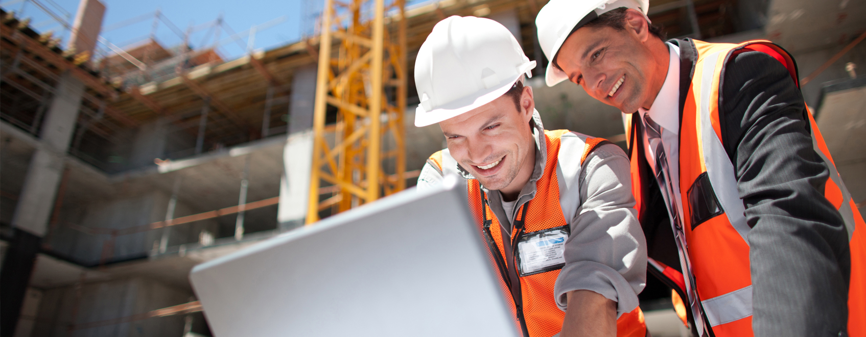 Construction team at work site smiling while looking at laptop together. 