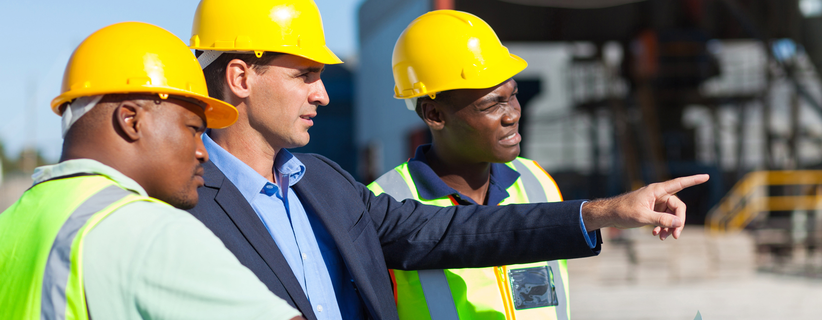 Three people in hard hats at construction site with the leader pointing out good work. 